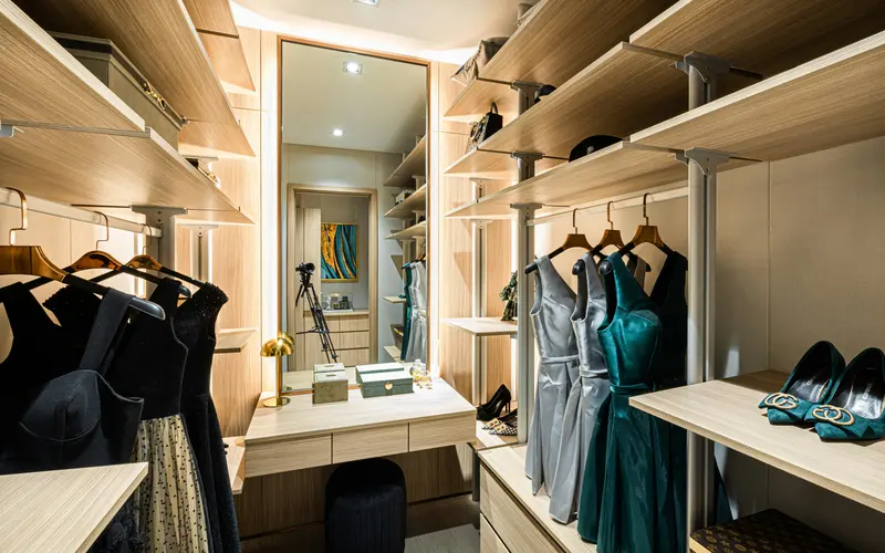 Closet em madeira clara com espelho, cabideiros e prateleiras iluminadas